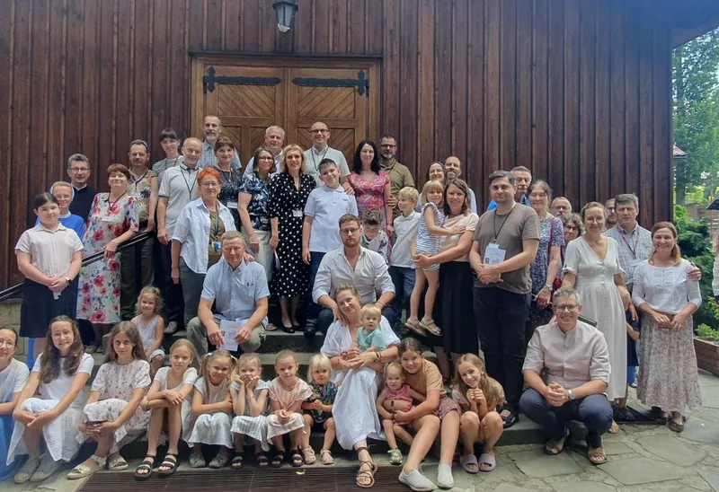 Duża grupa rodzin z dziećmi na schodach drewnianego kościoła podczas rekolekcji